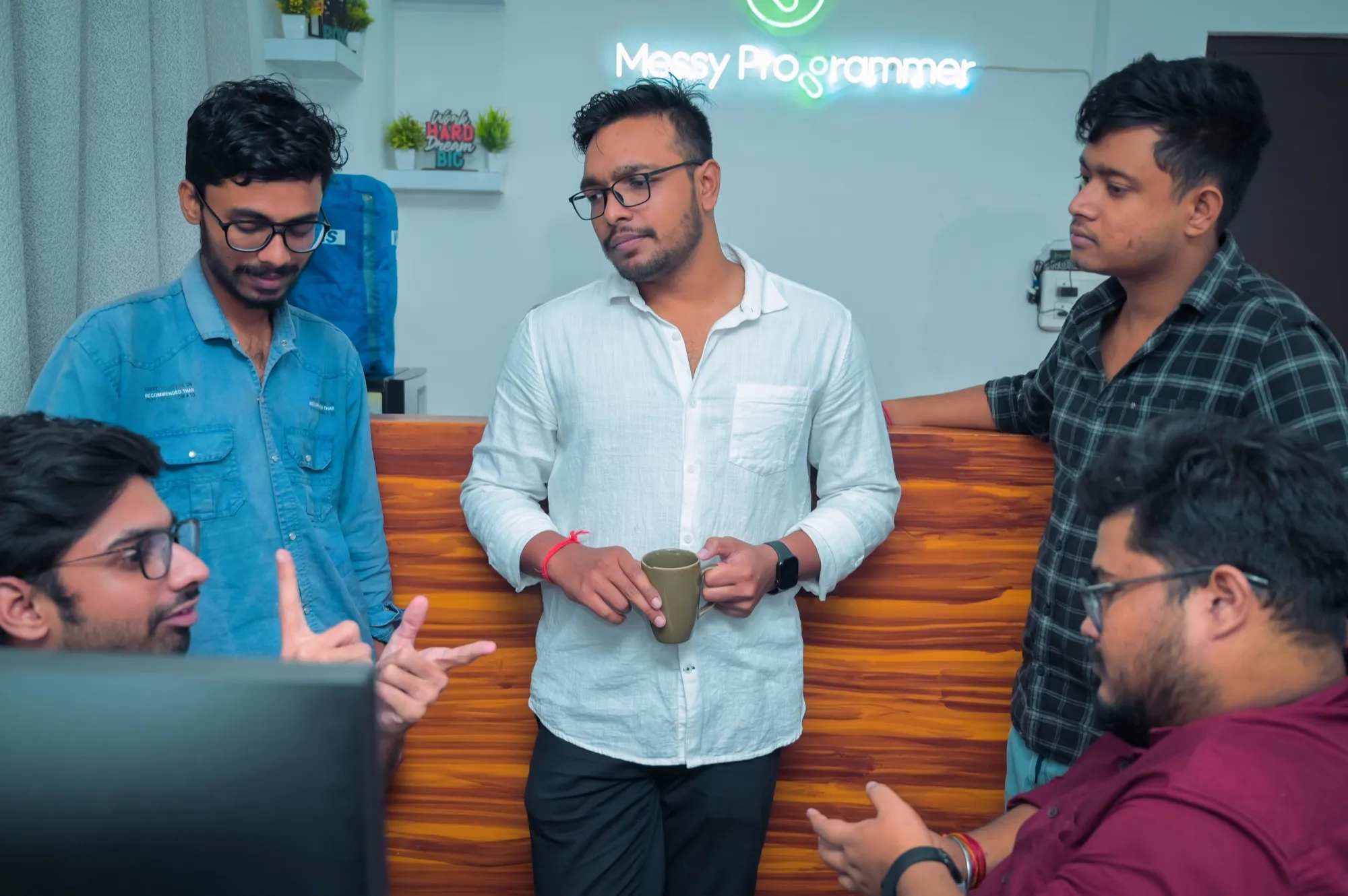 The Messy Programmer team gathered around a desk mid-discussion, under a neon studio sign.